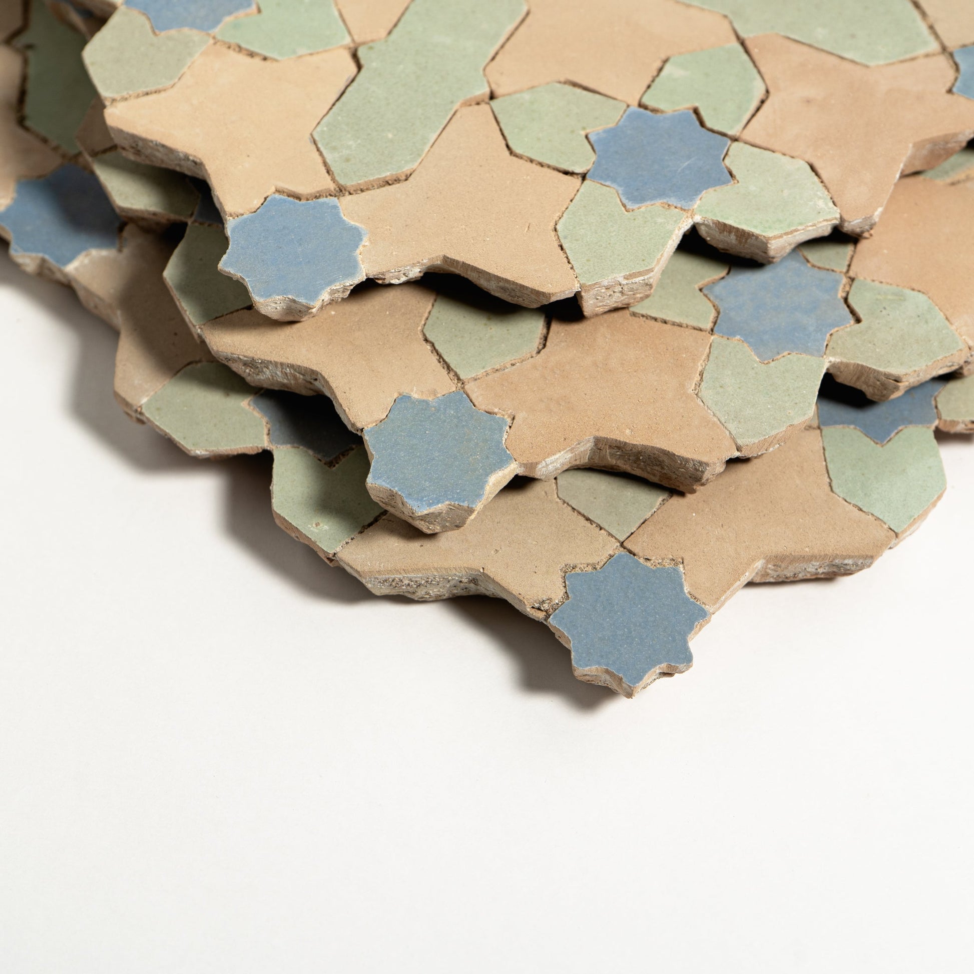 Stack of hexagonal ceramic tiles in beige, blue, and green on a white background